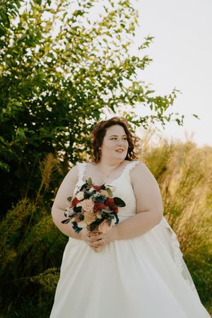 Bride in white dress holding floral bouquet during outdoor photo session.