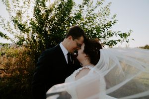 Couple sharing intimate moment during sunset wedding photos with trees in background.