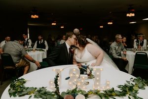 Wedding reception tables decorated with greenery and candles in dimly lit venue.