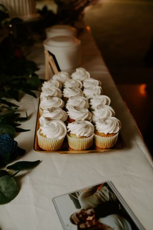 White frosted cupcakes arranged on white tablecloth for wedding dessert display.