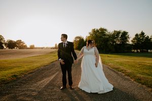 Newlyweds walk together on path during golden hour with dramatic sunset lighting.