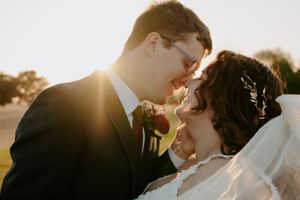 Wedding couple embraces in golden sunlight with flowing veil creating artistic silhouette.