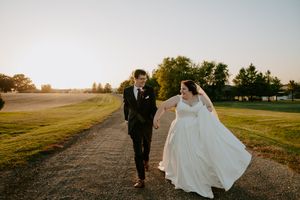 Wedding couple walks along country path with bride's dress flowing in evening light.