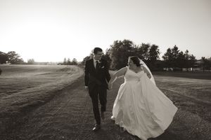 Black and white panoramic view of newlyweds walking along rural path at sunset.