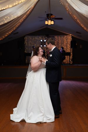Wedding couple dances together under draped fabric and string lights at indoor reception.