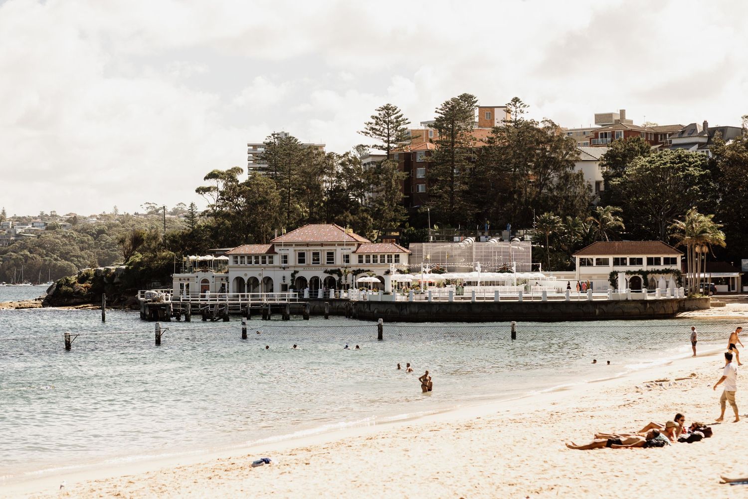 A panoramic view of a vintage beach scene with people relaxing on the sand and historic buildings along the shore.