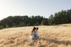 Romantic couple embracing in a sun-drenched hilltop meadow surrounded by pine trees.