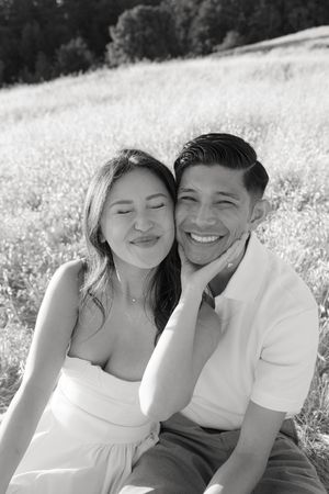 Black and white portrait of a couple sharing a tender moment in a sunlit meadow.