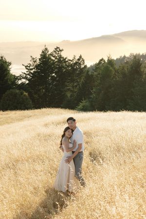 Couple sharing an intimate moment in a golden field during sunset with mountains in the distance.