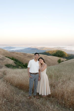 A couple poses together on a hillside overlooking misty mountain valleys at sunset.