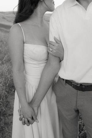 Black and white close-up of a couple in formal attire embracing in a meadow.