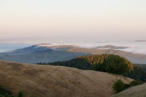 Misty mountain landscape at sunrise showing rolling hills and forested peaks.