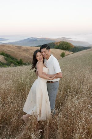 A couple in wedding attire embrace lovingly in a golden field of wild grass during sunset in the rolling hills.