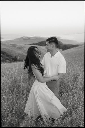 A romantic black and white photograph of a couple dancing in a hilltop meadow.