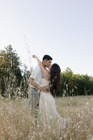 A romantic embrace captured in a golden meadow with towering evergreens.