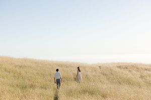 Two people walking through tall golden grass in a serene meadow landscape at sunset.