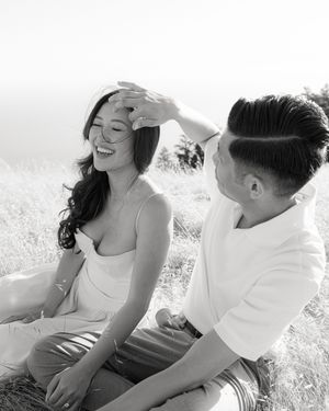 A black and white candid moment of a couple laughing together in a sunny field.