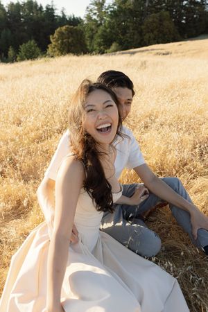 Joyful moment captured between two people sitting in a sun-drenched field of golden grass.