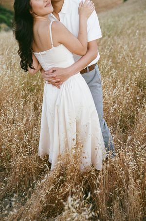 A couple embraces in a golden field of tall grass during a romantic photoshoot.