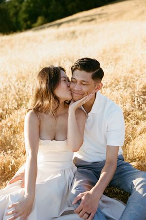Romantic couple sharing an intimate moment while sitting in a golden wheat field at sunset.