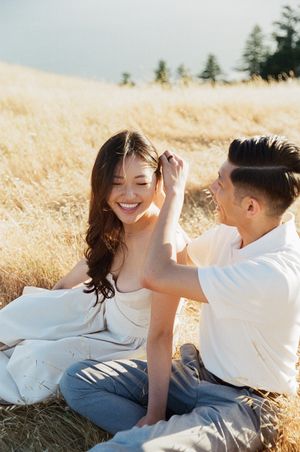 Couple lying together in a sunlit meadow sharing intimate moments during an outdoor photo session.