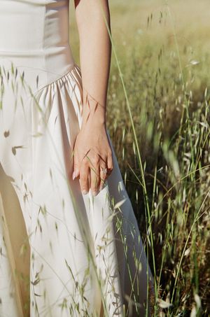 Close-up details of white dress and hands against natural grass backdrop during engagement photography.