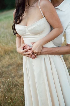 A romantic outdoor portrait showing clasped hands and a flowing cream-colored wedding dress with a sweetheart neckline.