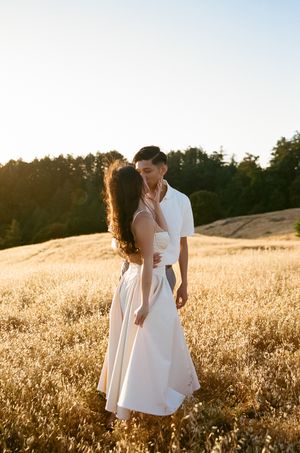 A couple embraces in a golden wheat field at sunset with warm backlighting creating a romantic silhouette.