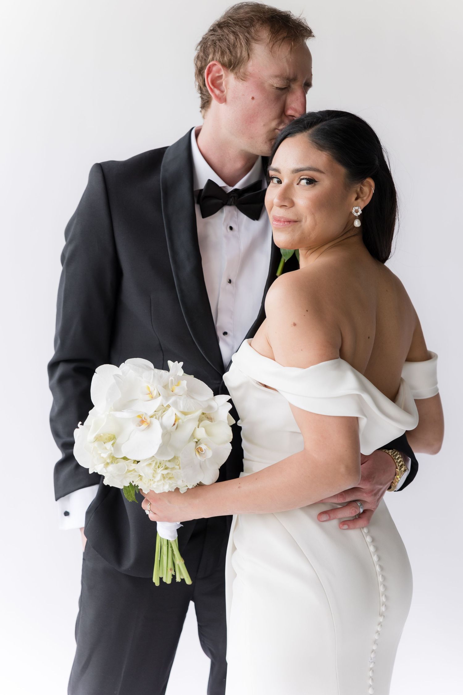 Wedding portrait featuring elegant white bridal gown and classic black tuxedo with white floral bouquet.