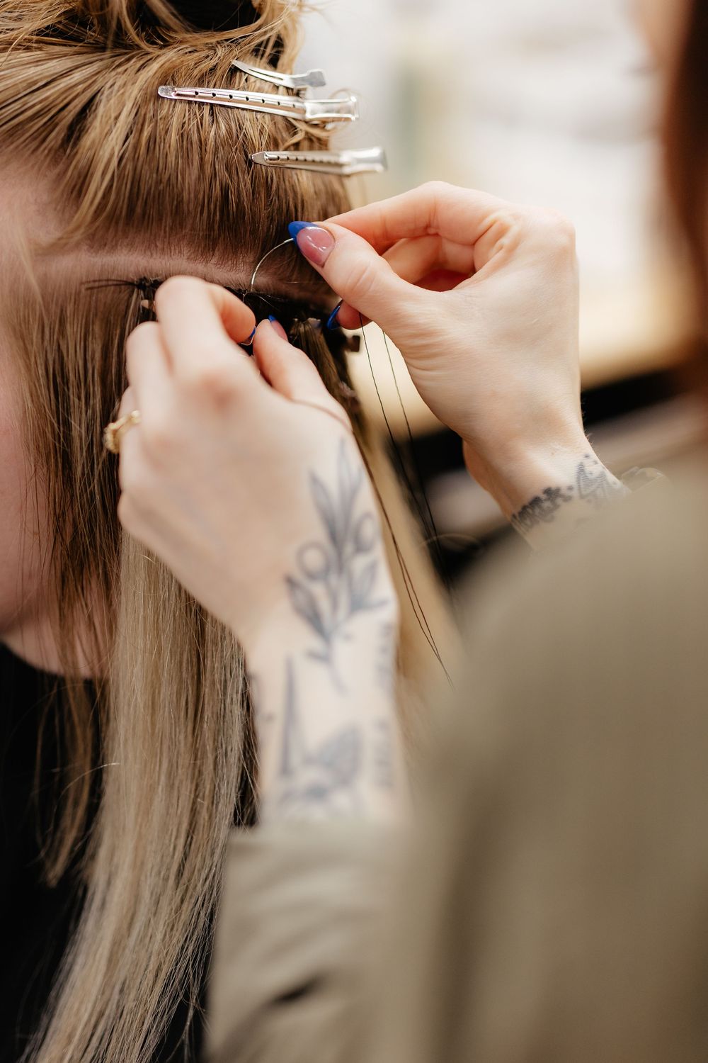 A hairstylist with tattooed hands carefully sections and clips blonde hair during a salon appointment.