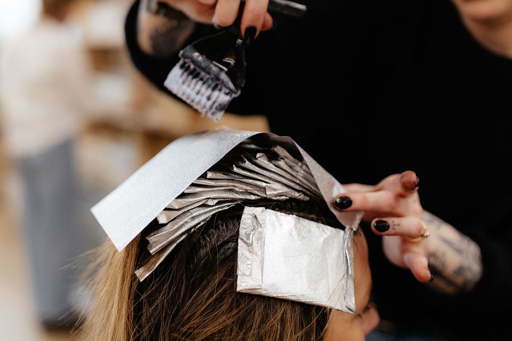 Hair stylist applying foils and bleach during a professional hair highlighting treatment at salon.