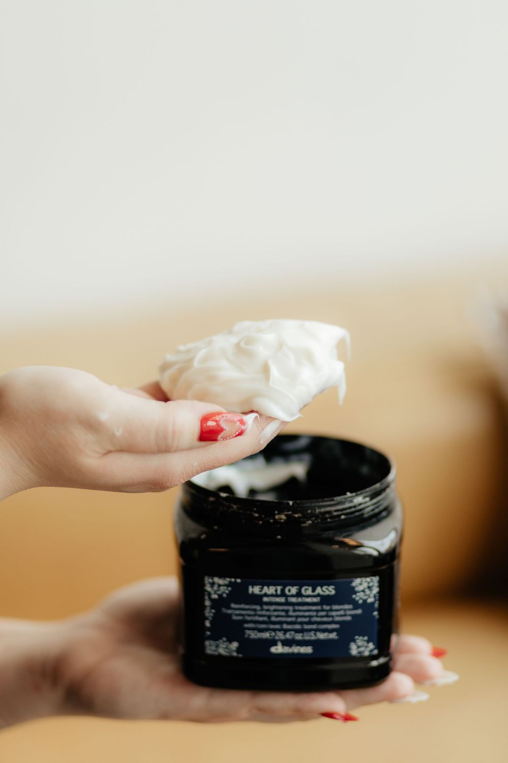 Hands with red nail polish opening a black beauty product jar with cream skincare product inside.