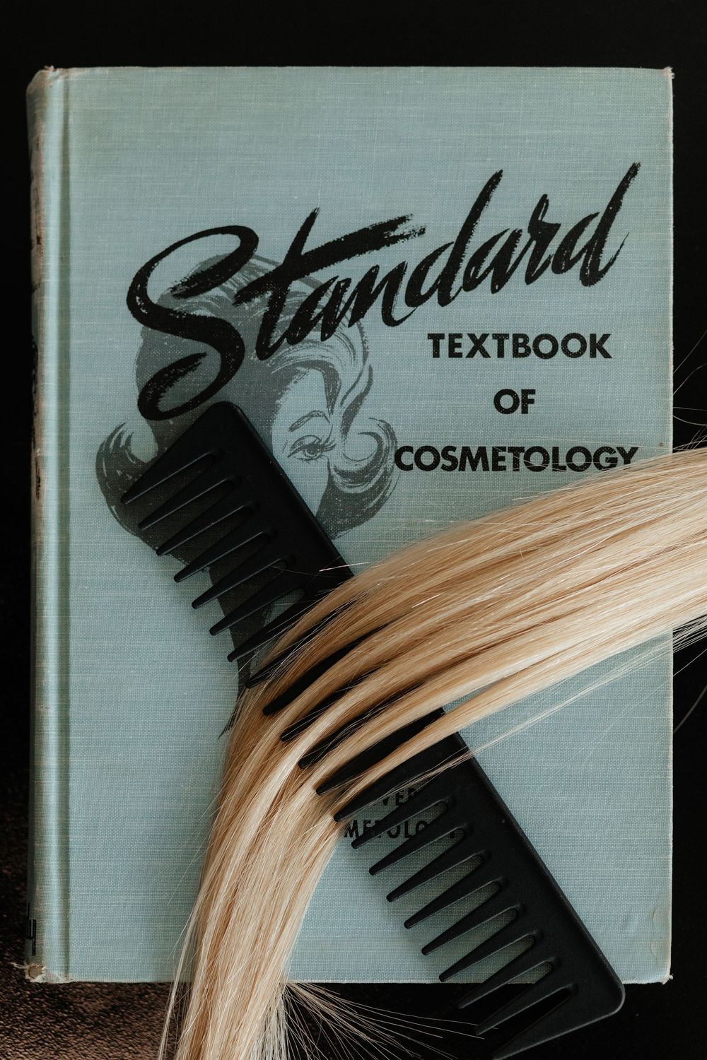 Black comb applying light blonde hair dye on white surface with textbook in background.