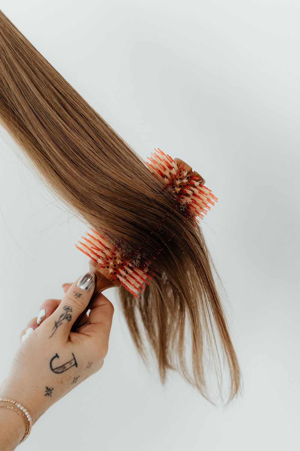 Hand with anchor tattoo brushing long brown hair with coral pink hairbrush in sequence on white background.
