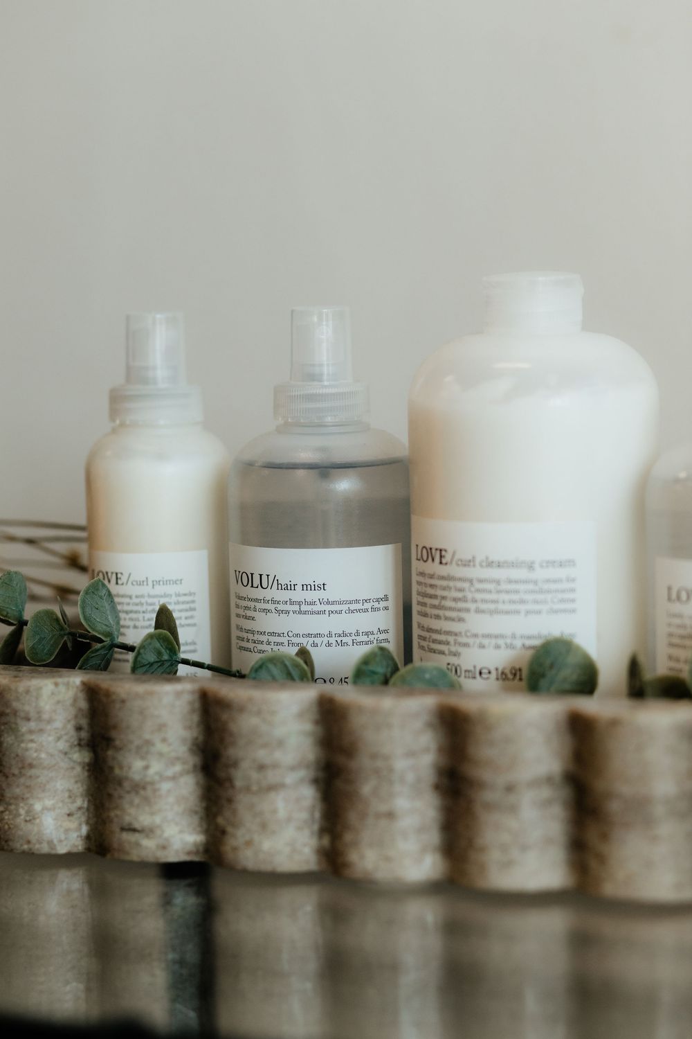 Skincare products lined up on wooden blocks with eucalyptus leaves, featuring minimalist white and clear bottles.