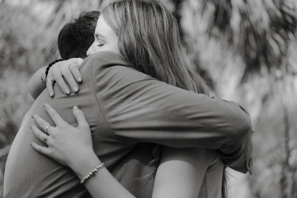 A tender black and white photo of two people embracing in an emotionally intimate moment outdoors.