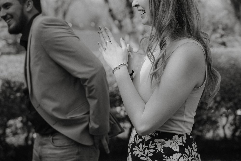 Black and white photo of a couple outdoors, one wearing a floral skirt laughs while the other looks away.