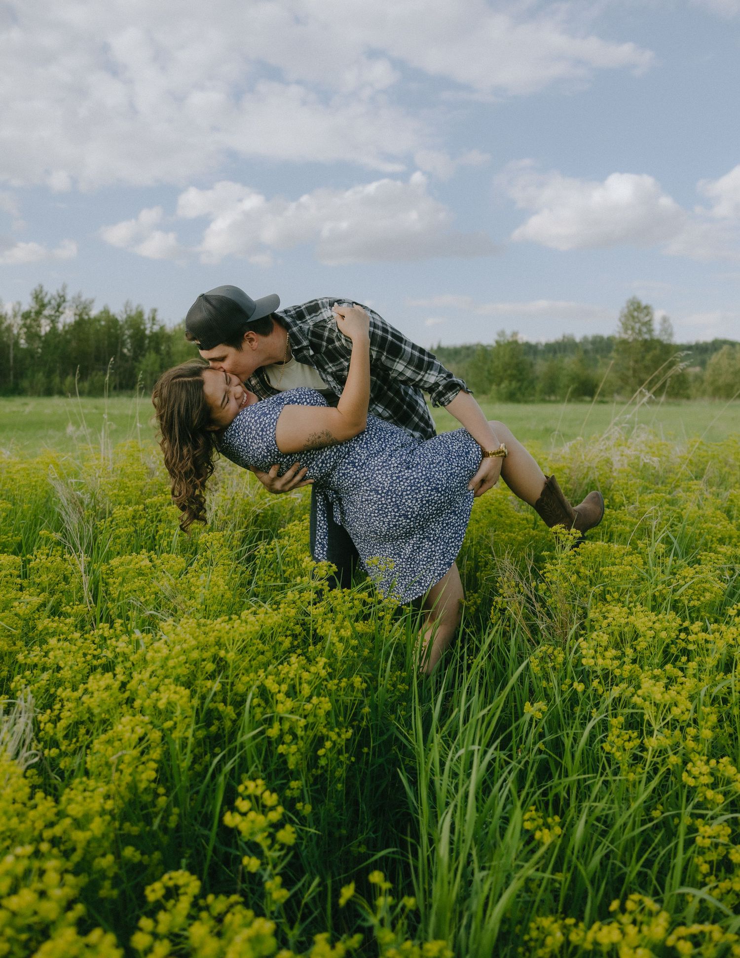 A romantic couple embraces playfully in a field of blooming yellow wildflowers.