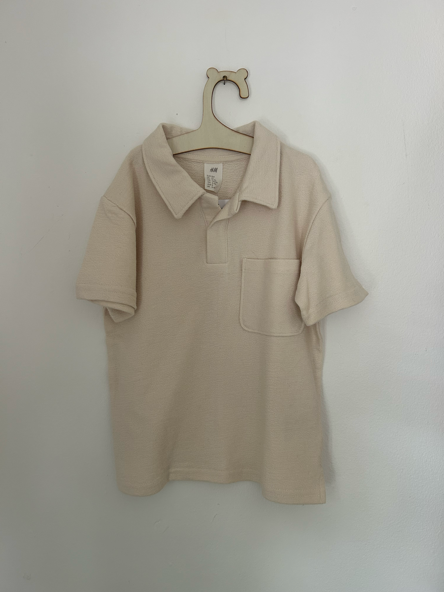 Vintage-style beige knitted baby romper with button details and side pockets hanging on display.