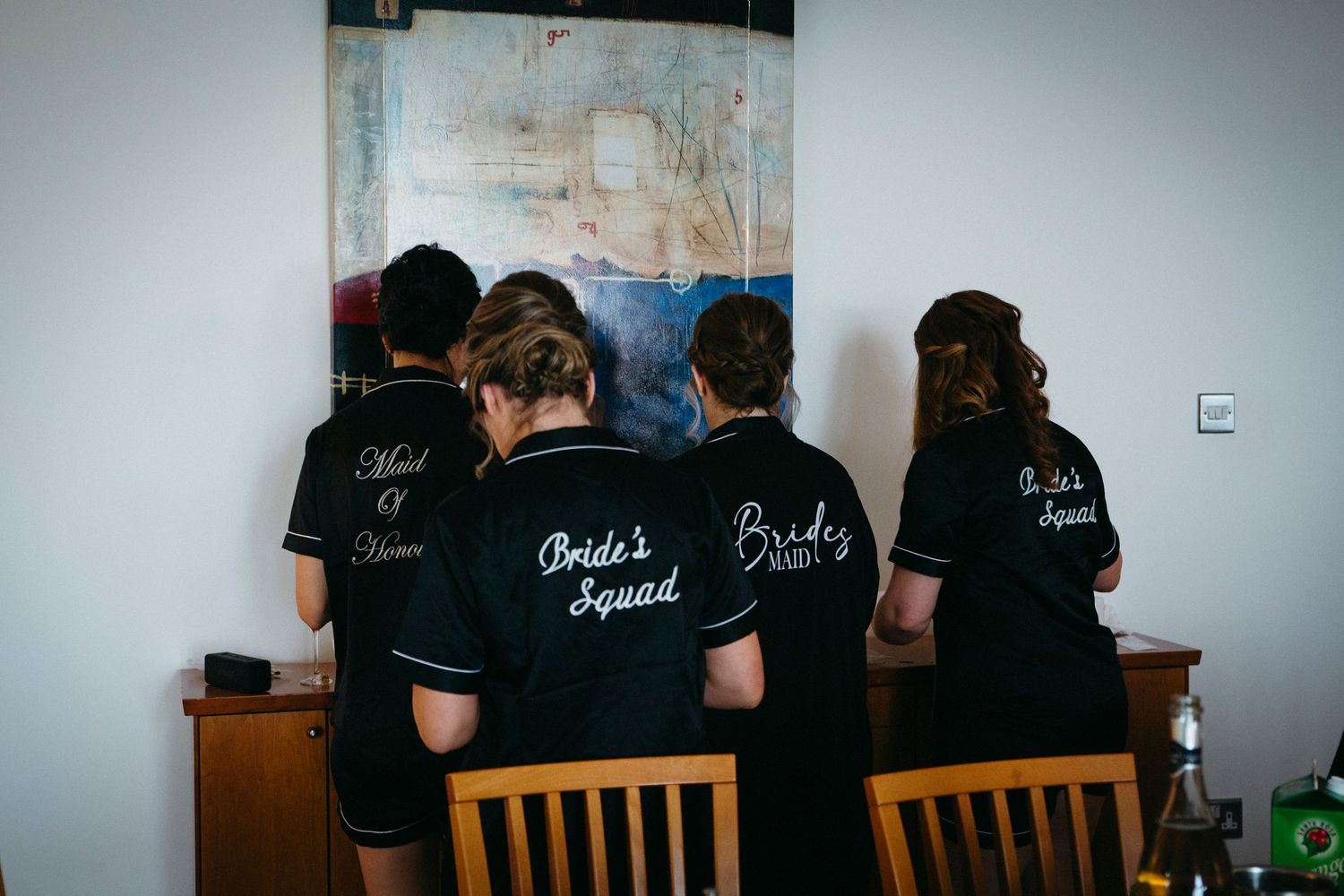 Group wearing matching black shirts with embroidered text standing together facing a wall art display.