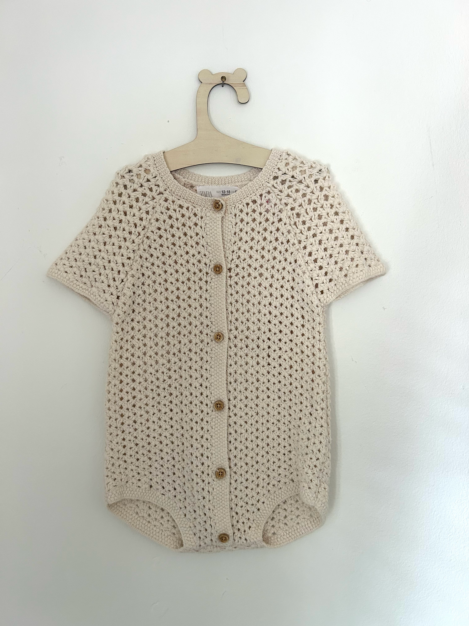 White knit baby romper with 'ONE' text and small bow detail in pink embroidery against hanging clothing background.