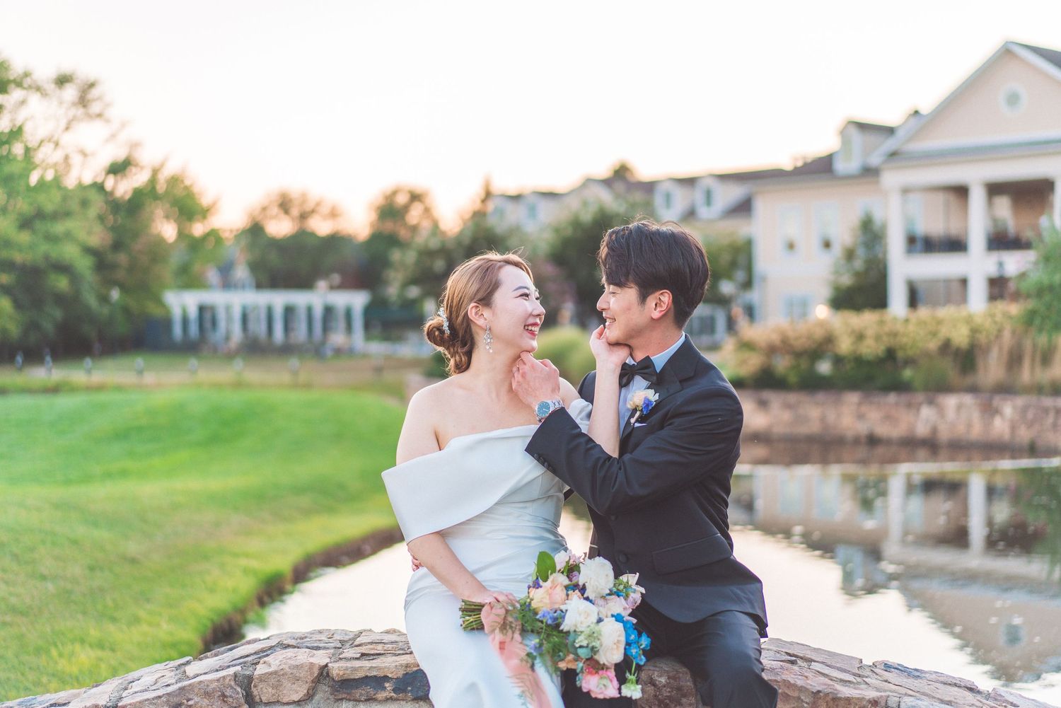 Wedding couple sharing a joyful moment by a reflective pond at sunset.