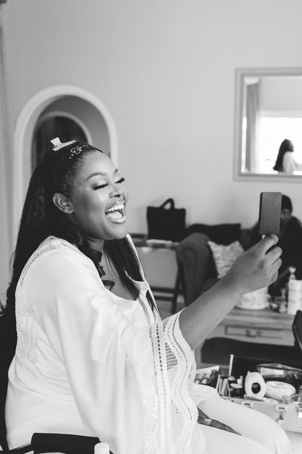 A candid black and white portrait shows a joyful smile while wearing a white top with lace trim and delicate hair accessories.
