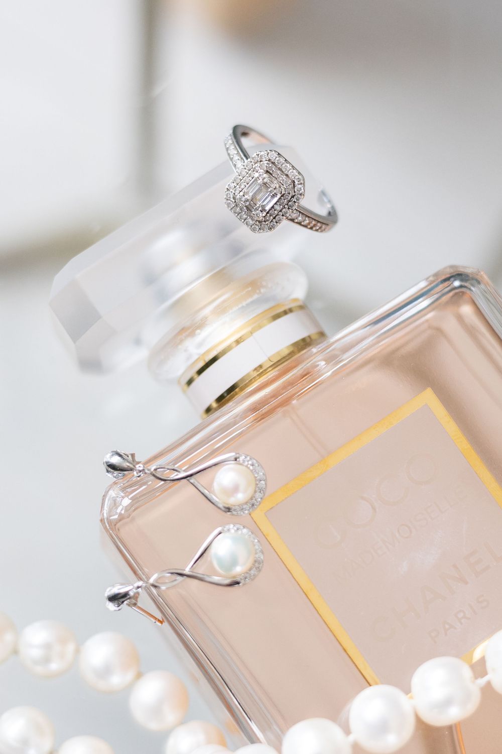 Elegant fragrance bottle with pearl and diamond jewelry in soft focus glamour photography style.