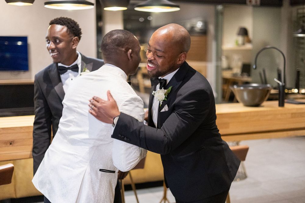 A touching moment at a wedding reception between people in formal attire, one in a white suit and another in a black suit.