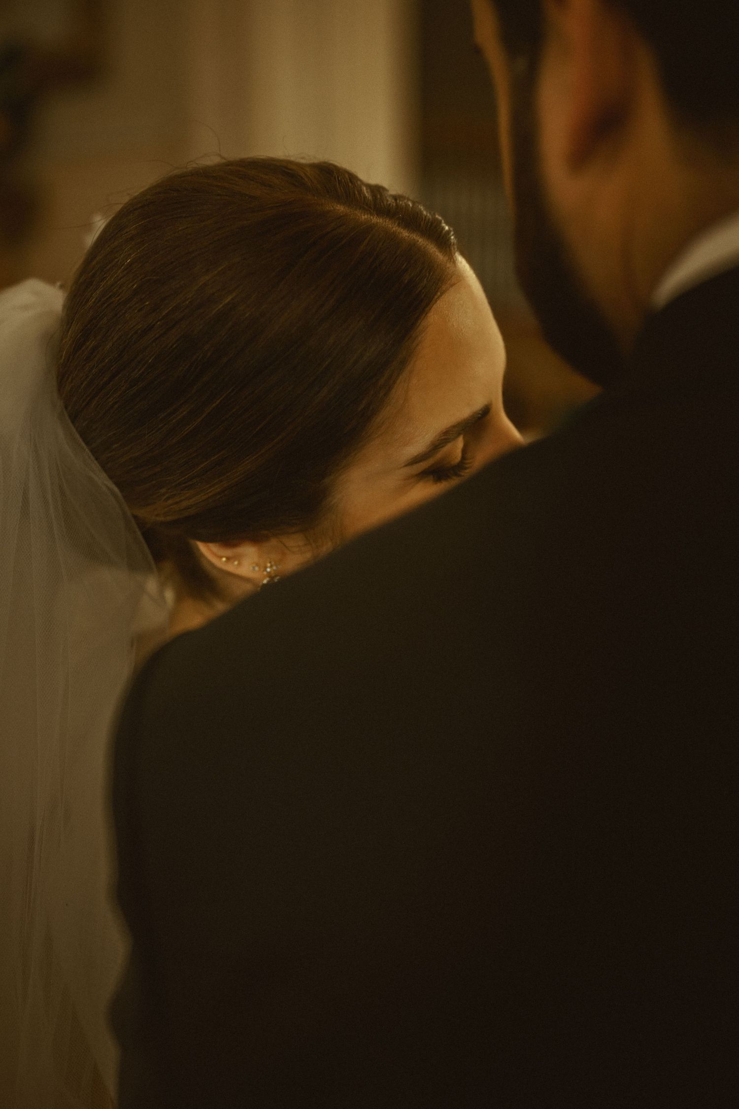An intimate wedding moment captured in warm lighting shows the bride in a veil looking over her shoulder with a gentle smile.