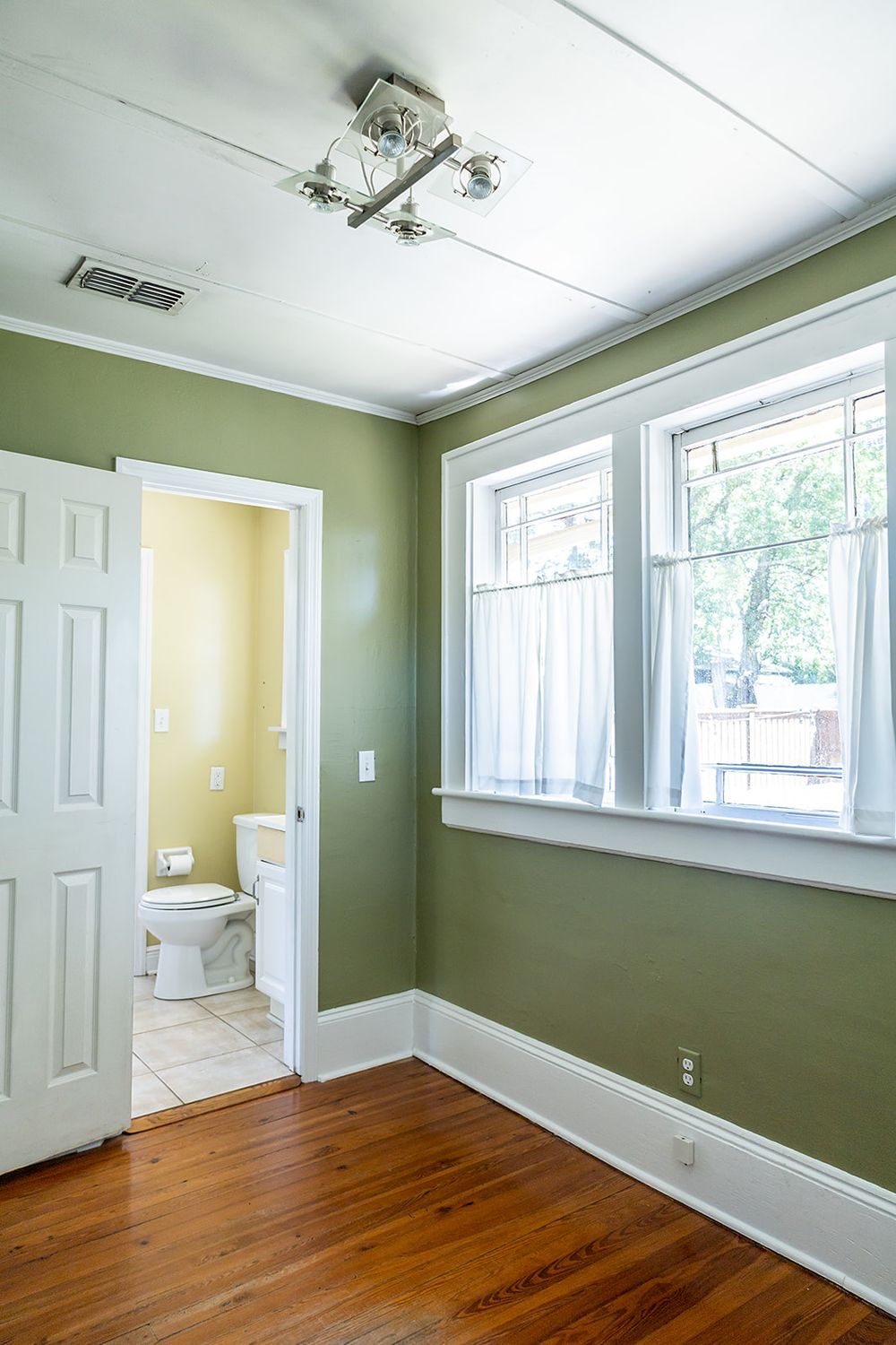 Empty room interior with hardwood floors, sage green walls, white trim, and natural light coming through window.