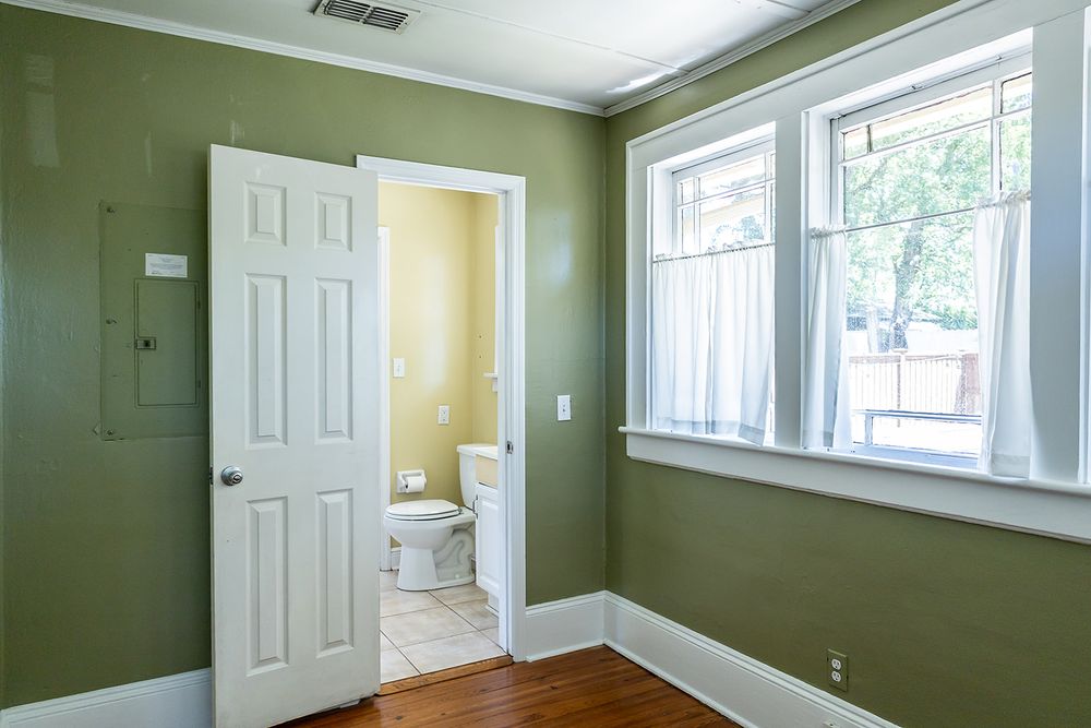 Empty room interior with sage green walls, white trim and multiple windows providing natural light.