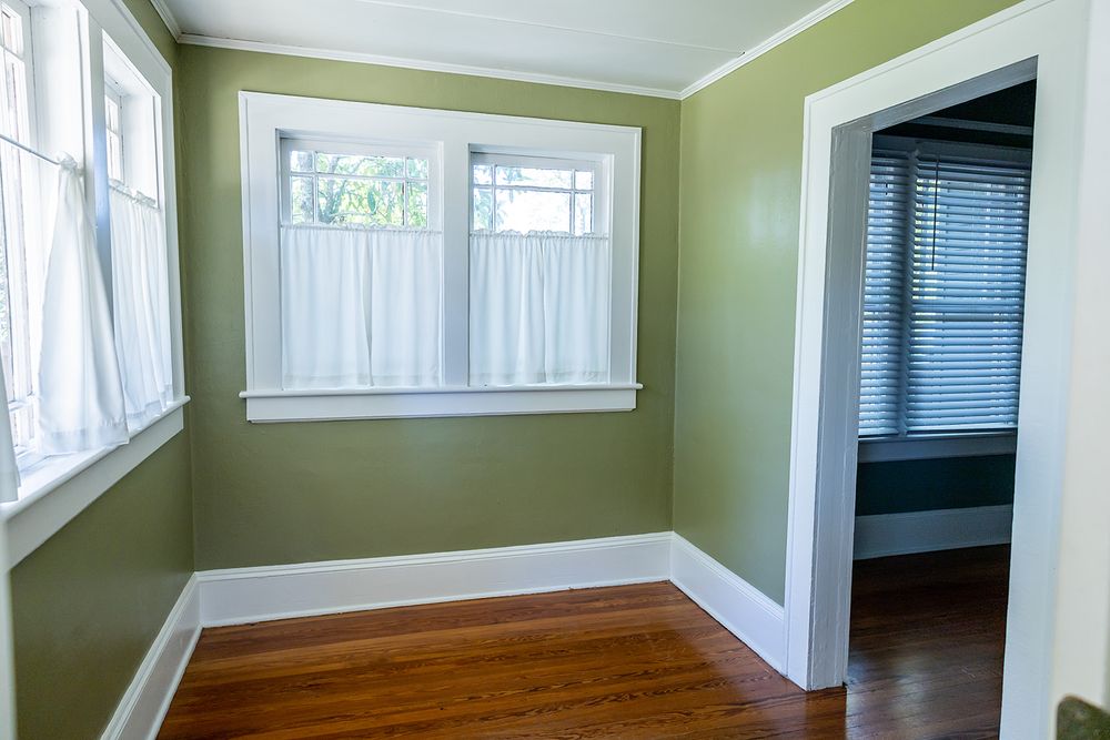 Empty room interior with light green walls, hardwood flooring, and multiple windows providing natural lighting.