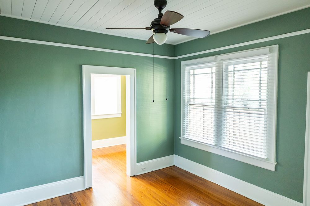 Empty room with sage green walls, hardwood floors, white trim, and two windows featuring natural light streaming in.